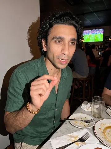 Denis, AI character: a crowded Spanish bar in Miami after work, Valencia match highlights on a TV behind him and small plates…