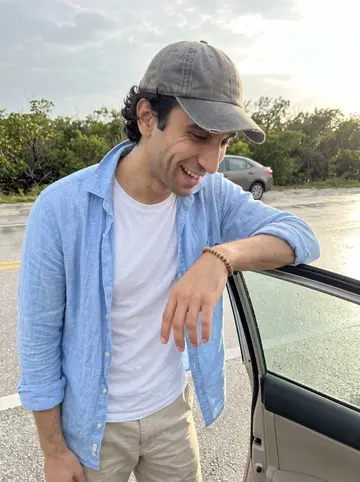 Denis, AI character: a roadside stop on the way back from the Florida Keys, wet pavement and low mangroves behind a parked…