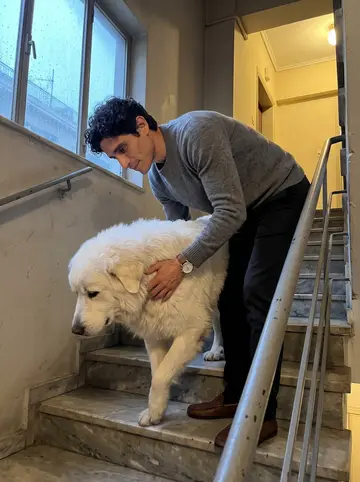 Theofilos, AI character: the stairwell of his Pangrati apartment building on a rainy spring evening, old marble steps and metal railing
