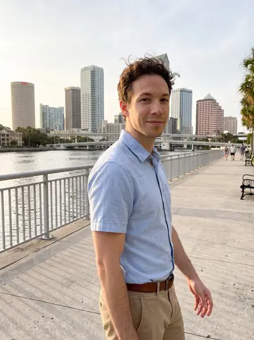 Aurelio, AI character: Tampa Riverwalk near the water just before sunset, downtown towers and the Hillsborough River behind him