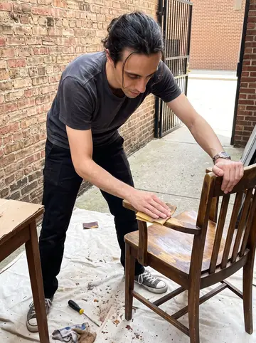 Achilleas, AI character: the open back area of his apartment building where he restores a curbside wooden chair on a drop cloth