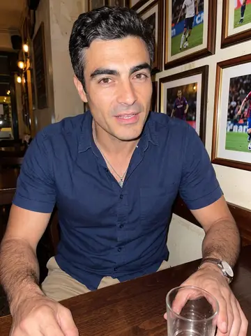 Cândido, AI character: small Portuguese bar in New Bedford after a soccer match, dark wood table and framed sports photos behind him