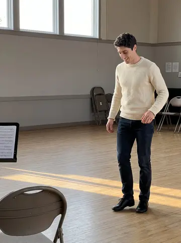 Mikel, AI character: community hall rehearsal for a Basque jota troupe, wooden floor, folding chairs, music stand near the wall