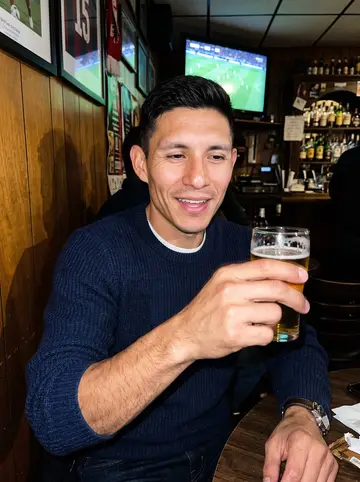 Tadeu, AI character: old Portuguese bar in the Ironbound during a Benfica match, warm wood wall and TV glow behind him