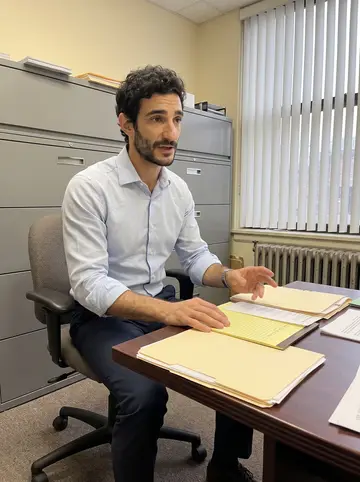 Athanasios, AI character: small three-lawyer immigration office in Chicago, squeezed between file cabinets, case folders, and a…