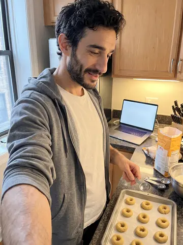 Athanasios, AI character: small Chicago apartment kitchen on a weekend morning, laptop open on the counter for a video call with his…