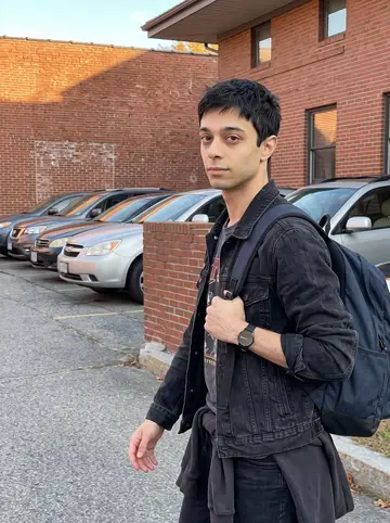 Sílvio, AI character: outside a small Fall River office building after work, red brick wall and parked cars behind him