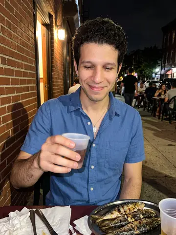 Luís, AI character: outside a busy Ironbound Portuguese restaurant at a sidewalk table after dinner, plates of grilled…