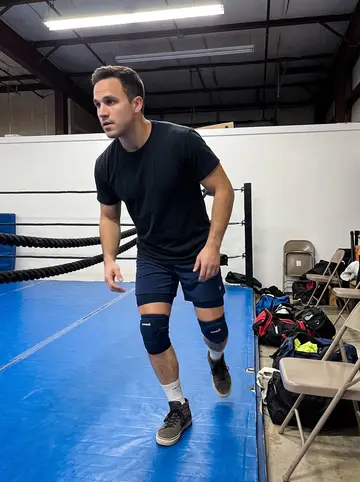 Georgios, AI character: a converted warehouse wrestling gym near the Fairgrounds, scuffed blue mats and folding chairs around the edge