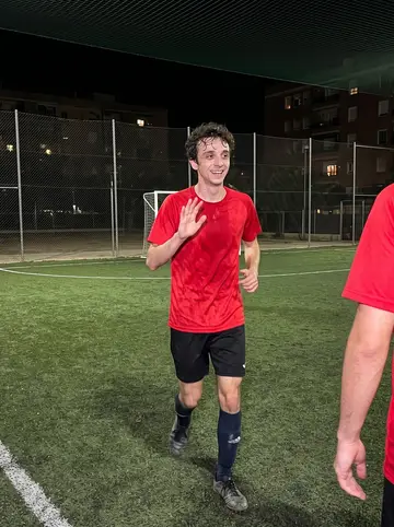 Zacarias, AI character: a small outdoor five-a-side football court in Valencia after work, chain-link fence and dark apartment…