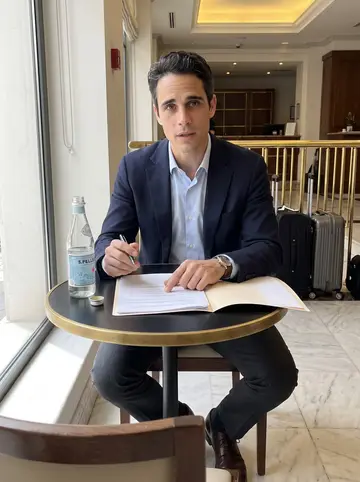 Ioannis, AI character: a quiet back corner of an Athens hotel lobby cafe between meetings, marble floor, brass railings and guest…