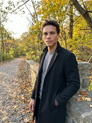 Ezra, AI character: a low stone wall beside Forbidden Drive in Wissahickon Valley Park, Philadelphia, late afternoon, fallen…