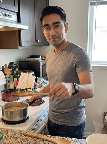 Joshua, AI character: his Daly City apartment kitchen on a Sunday morning, recipe card on the counter beside a simmering pot