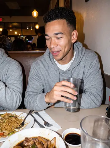 Malcolm, AI character: a casual Filipino restaurant in Vallejo at night, crowded table with friends, plates of pancit and adobo…