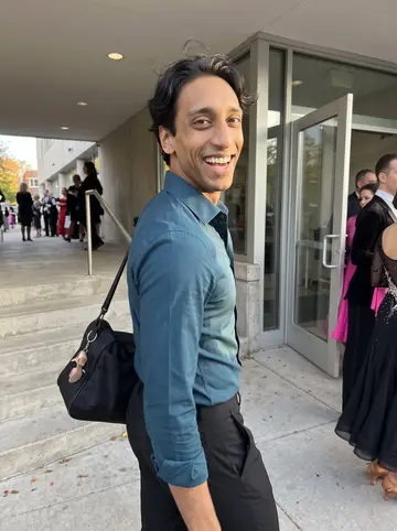 Raymond, AI character: outside a community ballroom competition venue after afternoon practice, glass doors and a few dressed-up…