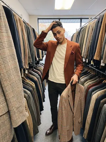 Tyrone, AI character: a narrow South Street thrift store aisle packed with vintage blazers, suit hangers, and a cloudy front window