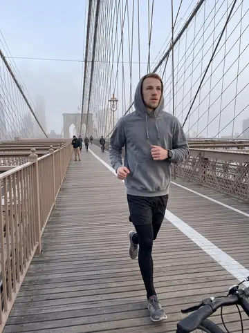 Toby, AI character: Brooklyn Bridge pedestrian path just after dawn, fog softening the skyline and a few commuters in the distance