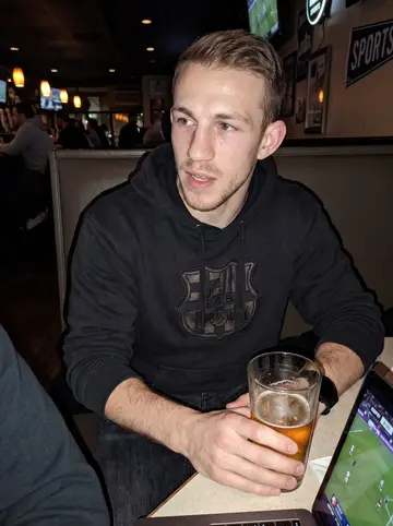 Toby, AI character: a crowded New York sports bar at 3am with a Sheffield United match playing on a laptop at the table