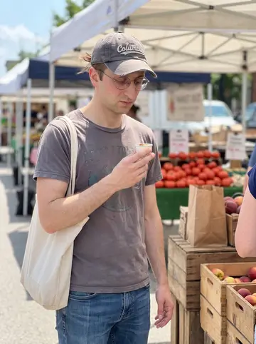 Craig, AI character: a Saturday farmers market in Columbus, produce stalls and tote bags around him