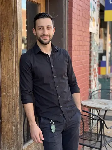 Muhammad, AI character: outside the Cherokee Street bar before opening, standing in the side doorway with the painted brick wall…