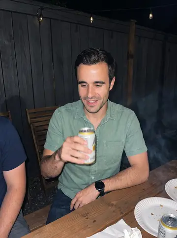 Brayden, AI character: casual backyard cookout in Wallingford, friends cropped around him at a picnic table with paper plates and…