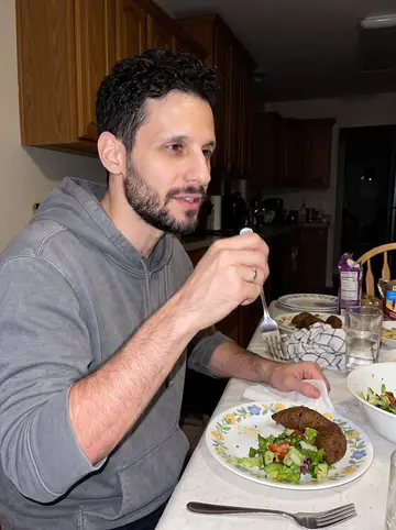 Kareem, AI character: his mother's Dearborn kitchen during a late family dinner, plates of kibbeh and salad crowded on the table