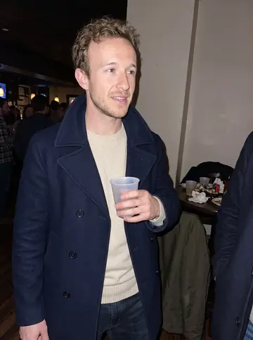 Jackson, AI character: a small Cleveland bar during an alumni reunion mixer, crowded tables and coats on chair backs behind him