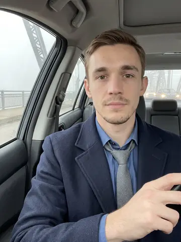 Jasper, AI character: parked car before work near the Liberty Bridge, damp windshield and Pittsburgh traffic blurred behind him