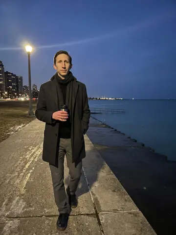 Peter, AI character: the Chicago lakefront path after work, dark water and distant apartment lights behind him, a small thermos…