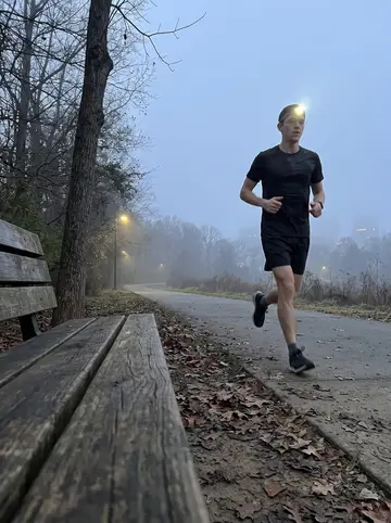 Todd, AI character: Little Sugar Creek Greenway before dawn, fog over the path, phone propped on a park bench beside the trail