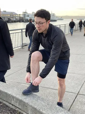Seth, AI character: near the Seattle ferry dock after his morning run, cold blue water and commuters in coats behind him