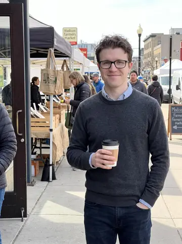 Zachary, AI character: outside a small cafe near the Madison farmers market on a clear Saturday morning, stalls and early…