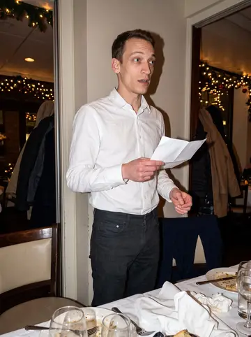 Andy, AI character: a small restaurant private room during his sister's wedding-planning dinner, string lights and coats on…