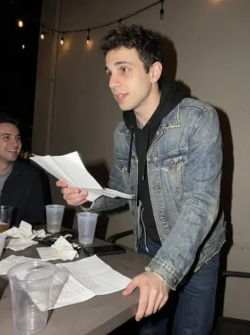 Enrique, AI character: a casual Sacramento bar patio during a pre-wedding hangout, plastic cups and folded speech notes on the table