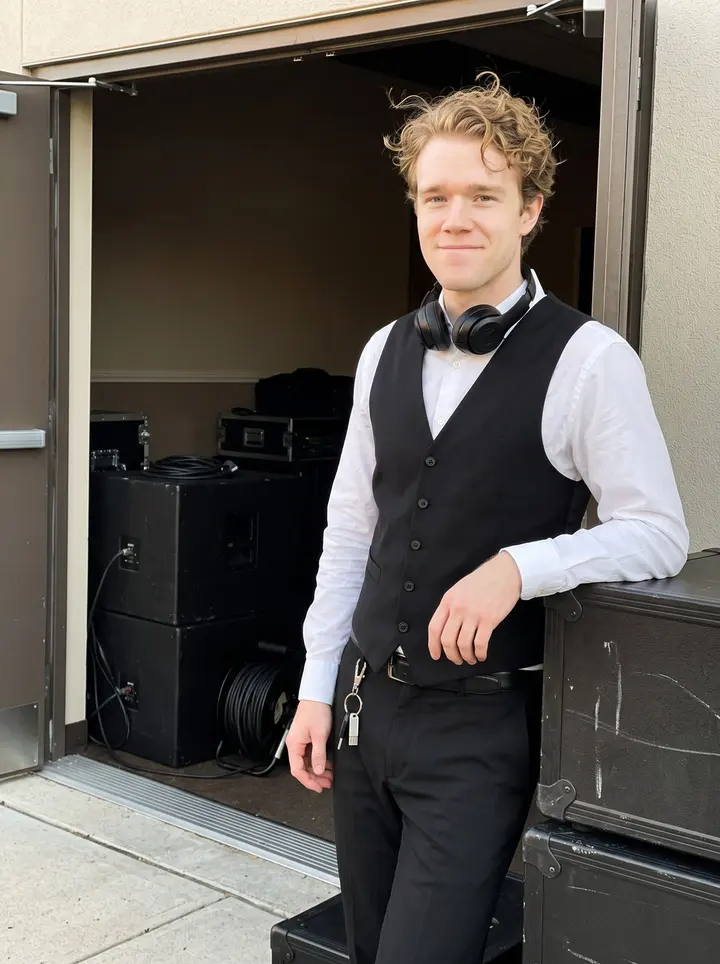 Charlie, AI character: outside a Scranton reception hall during golden hour, standing in the side doorway near stacked speaker…