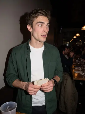 Dillon, AI character: a crowded Logan Square bar during his monthly pub trivia night, standing near the end of a long wooden table