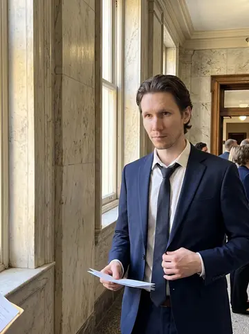 Donovan, AI character: courthouse hallway in Savannah before a small Saturday wedding, old marble wall and tall window beside him