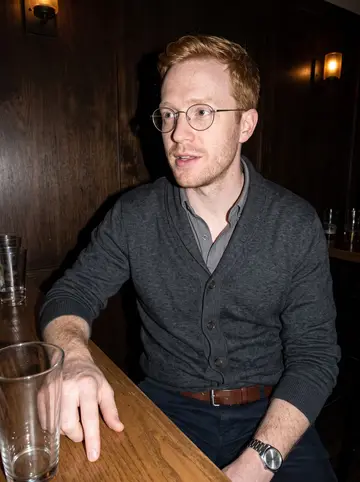 Scott, AI character: a quiet Minneapolis bar after a community fundraiser, dark wood wall and half-empty glasses behind him