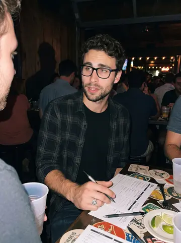 Stephen, AI character: a crowded trivia night at a Rainey Street bar, standing beside a high table with answer sheets and plastic…