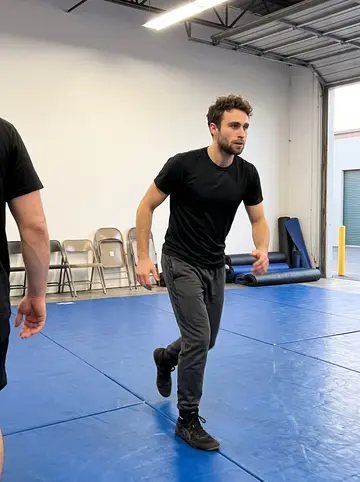 Stephen, AI character: Thursday night wrestling training inside a rented warehouse gym, blue practice mats and folding chairs…