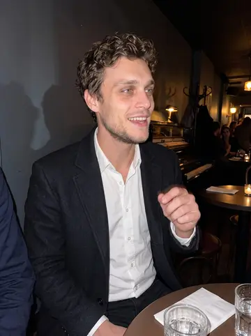 John, AI character: a crowded basement piano bar after a hospital fundraiser, small round tables and a piano in the background