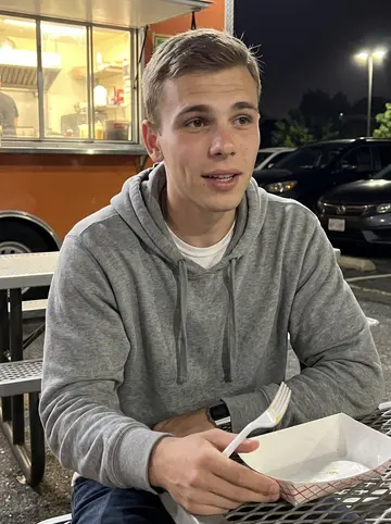 Bobby, AI character: outside a taco truck near Riverside Drive in Tulsa, metal picnic tables and parked cars behind him