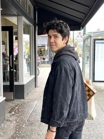 Amir, AI character: a Vancouver side street outside the corner café after his shift, cherry blossoms on the wet sidewalk and a…