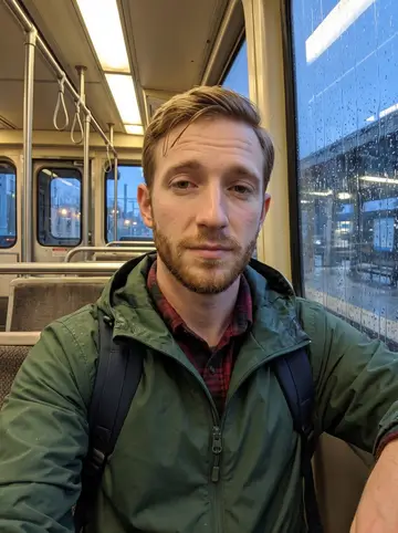 Kirk, AI character: inside a Cleveland RTA train car after work, wet window and blurred station lights behind him