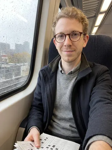 Kaleb, AI character: a commuter train seat by a rainy window between Madison and the office, crossword folded on his lap