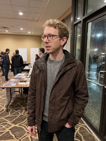 Kaleb, AI character: a local fan convention hotel lobby after rain, with blank banners, folding tables, and people blurred in…