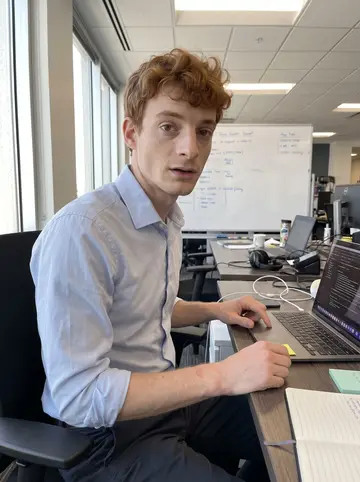 Warren, AI character: his Denver tech office near a shared desk, laptop open beside a whiteboard with only blurred shapes