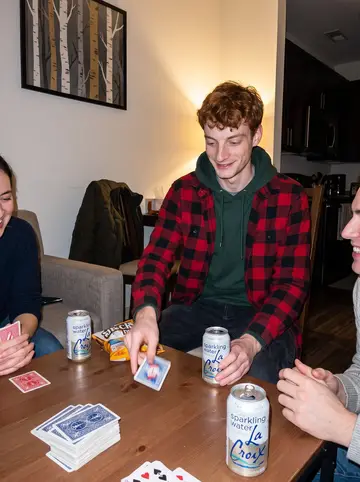 Warren, AI character: a neighbor's apartment game night, crowded table with cards, snacks, and cans of sparkling water