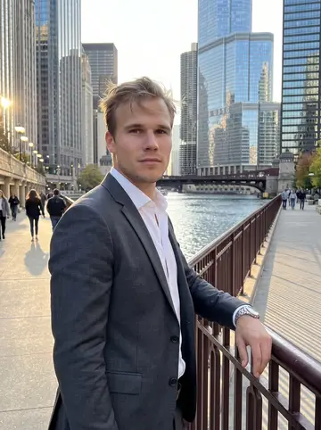 Finley, AI character: the Chicago Riverwalk after work, standing by the railing with glass towers and autumn light behind him