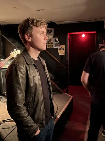 David, AI character: small Scranton basement punk show, low stage, black walls, old flyers near the stairs